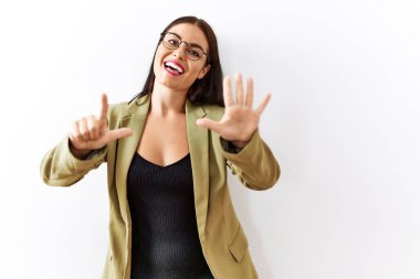 Genç esmer kadın izole edilmiş arka planda duruyor. Yedi numaralı parmaklarıyla işaret ediyor ve gülümsüyor. Kendinden emin ve mutlu.. 