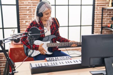 Middle age grey-haired woman musician playing electrical guitar at music studio