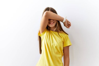 Young brunette teenager standing together over isolated background covering eyes with arm smiling cheerful and funny. blind concept. 