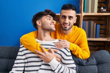 İki erkek, evdeki kanepede oturup birbirlerine sarılıyorlar.