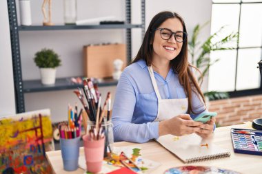 Sanat stüdyosunda akıllı telefon çizimi yapan genç bir kadın sanatçı.
