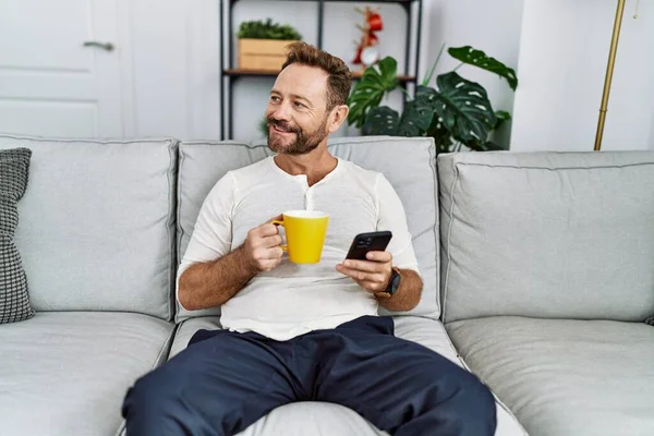 中年パニック男使用スマートフォン飲料コーヒーに自宅 — ストック写真