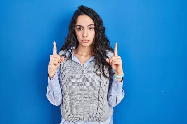 Jovem Morena Sobre Fundo Azul Apontando Para Cima Olhando Triste — Fotografia de Stock