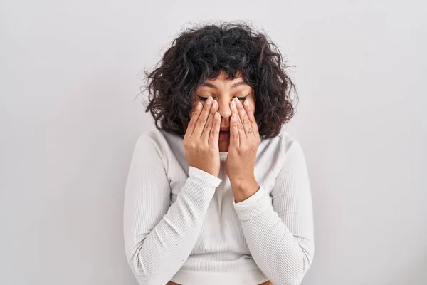 Hispanic woman with curly hair standing over isolated background rubbing eyes for fatigue and headache, sleepy and tired expression. vision problem