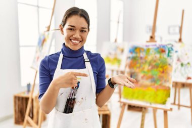 Sanat stüdyosundaki genç esmer kadın kameraya hayret ediyor ve gülümsüyor.. 