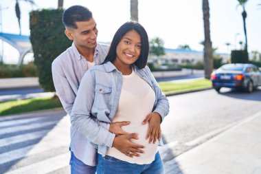 Latin bir çift bebek bekliyor. Sokakta birbirlerine sarılıyorlar.