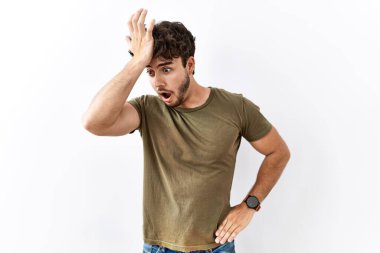 Hispanic man standing over isolated white background surprised with hand on head for mistake, remember error. forgot, bad memory concept. 