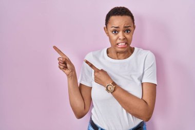 Güzel Afro-Amerikan kadını pembe arka planda dikiliyor. Endişeli ve gergin olduğunu gösteriyor. Endişeli ve şaşırmış ifade. 