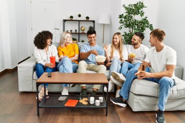 Mutlu bir şekilde gülümseyen bir grup genç arkadaş evde film izliyor..