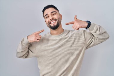 Soyutlanmış arka planda duran, neşeli gülümseyen ve parmaklarıyla ve ağzıyla işaret eden genç yakışıklı bir adam. Diş sağlığı konsepti. 