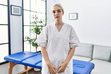 Young caucasian physiotherapy woman working at home with serious expression on face. simple and natural looking at the camera. 