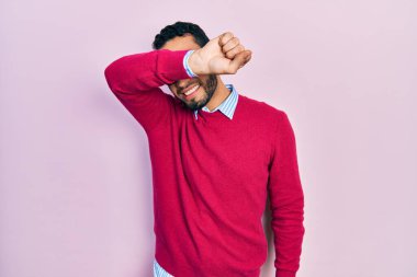 Hispanic man with beard wearing business shirt and glasses covering eyes with arm, looking serious and sad. sightless, hiding and rejection concept 