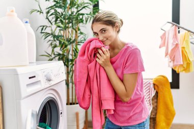 Çamaşırhanede elbise kokusu alan beyaz bir kadın.