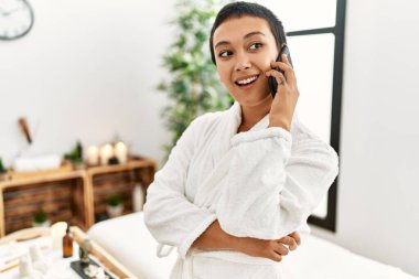 Bornoz giyen genç İspanyol kadın güzellik merkezinde akıllı telefondan konuşuyor.