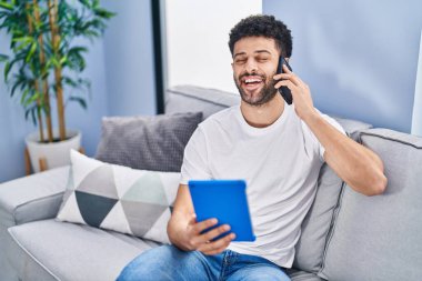 Genç Arap adam akıllı telefondan konuşuyor. Evdeki kanepede oturuyor.