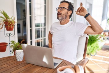 Middle age man using computer laptop at home stretching back, tired and relaxed, sleepy and yawning for early morning 