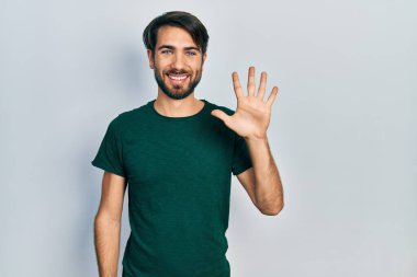 Gündelik beyaz tişört giyen genç İspanyol adam beş numarayı gösterip işaret ederken kendinden emin ve mutlu gülümsüyor.. 