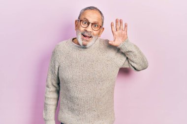 Handsome senior man with beard wearing casual sweater and glasses waiving saying hello happy and smiling, friendly welcome gesture 