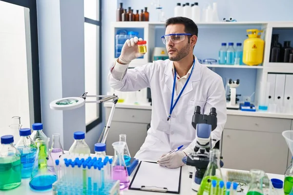 Young Hispanic Man Scientist Looking Urine Test Tube Writing Report — Stockfoto