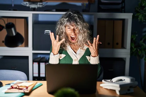 コンピュータのラップトップを使用して夜に働く中年の女性は狂気と怒鳴り声を上げ 積極的な表現と腕を上げて叫びました フラストレーションコンセプト — ストック写真