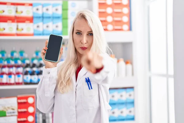 Caucasian Woman Working Pharmacy Drugstore Showing Smartphone Screen Pointing Finger — Zdjęcie stockowe
