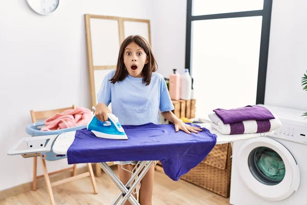 Young Hispanic Girl Ironing Clothes Laundry Room Scared Amazed Open — 스톡 사진