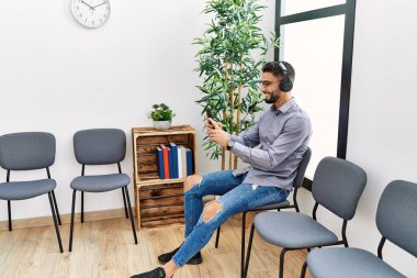 Genç Arap adam bekleme odasında oturmuş müzik dinliyor.
