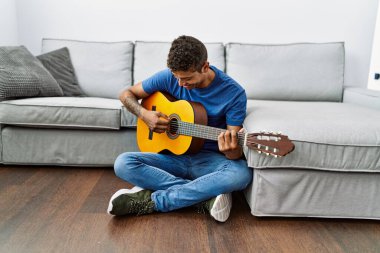 Gitar çalan genç İspanyol adam evde yerde oturuyor.