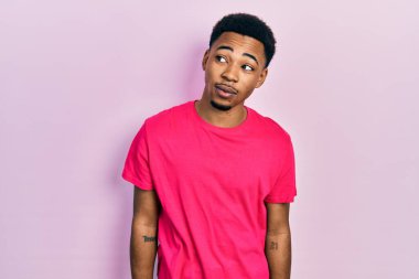 Genç Afrikalı Amerikalı adam Casua tişörtü giyiyor. Gülümsüyor, yan tarafa bakıyor ve düşünüyor.. 