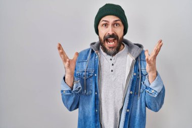 Young hispanic man with tattoos wearing wool cap celebrating crazy and amazed for success with arms raised and open eyes screaming excited. winner concept 