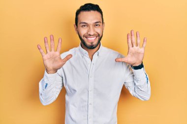 Hispanic man with beard wearing business shirt showing and pointing up with fingers number ten while smiling confident and happy. 