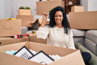 Orta yaşlı, İspanyol bir kadın elinde yeni evin anahtarlarını tutuyor. Pozitif ve mutlu görünüyor. Kendine güvenen bir gülümsemeyle dişlerini gösteriyor. 