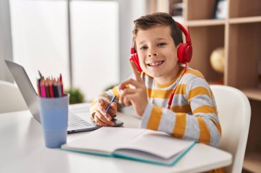 Evde ödev yapan beyaz bir çocuk bir fikre ya da soru işaretine şaşırmış ve mutlu bir yüzle işaret ediyor. 