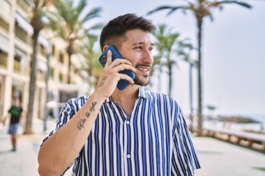 Genç yakışıklı adam deniz kenarında telefonla konuşuyor.