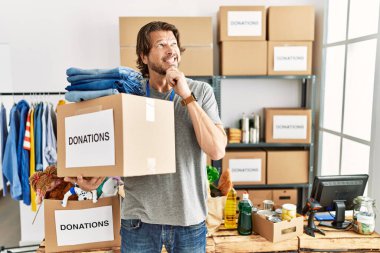 Handsome middle age man holding donations box for charity at volunteer stand thinking worried about a question, concerned and nervous with hand on chin 