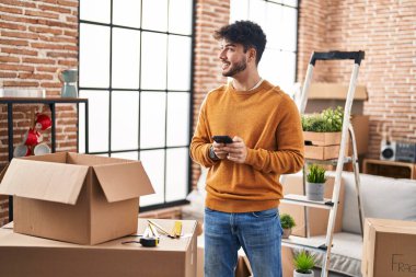 Young hispanic man smiling confident using smartphone at new home