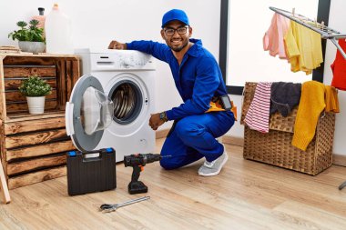 Young indian technician working on washing machine with a happy and cool smile on face. lucky person. 