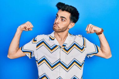 Sıradan kıyafetler giyen genç İspanyol adam gururla gülümseyen kol kaslarını gösteriyor. fitness konsepti. 