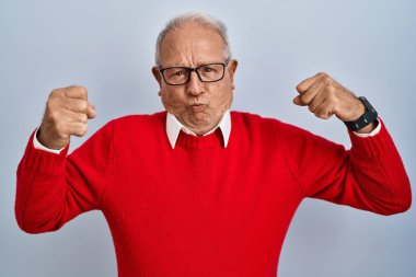 Senior man with grey hair standing over isolated background showing arms muscles smiling proud. fitness concept. 