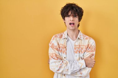 Gündelik yaz gömleği giyen, kuşkucu ve gergin genç bir adam yüzünde çapraz kollu tasvip etmeyen bir ifade var. negatif kişi. 