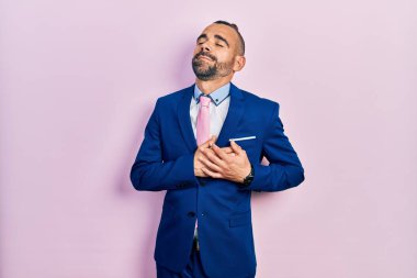 Genç İspanyol bir adam iş elbisesi ve kravat takıyor elleri göğsünde, gözleri kapalı gülümsüyor ve yüzünde minnet ifadesi var. sağlık kavramı. 