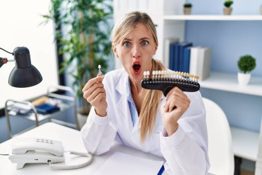 Beautiful dentist woman comparing teeth whitening in shock face, looking skeptical and sarcastic, surprised with open mouth 
