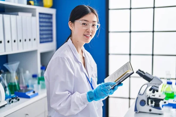 Chinese woman scientist smiling confident reading book at laboratory