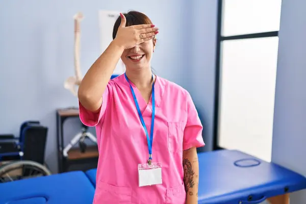 リハビリクリニックで働く若いブルネットの女性は笑顔で 驚きのために目を覆う顔で手で笑っています 視覚障害の概念 — ストック写真