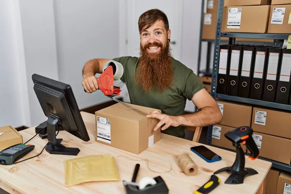 Young redhead man business worker packing carboard box at office