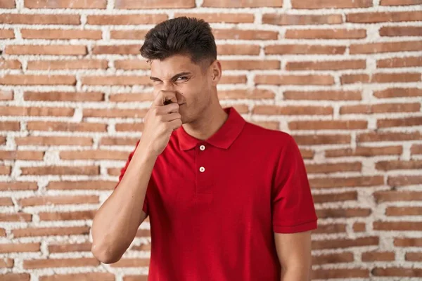 Young Hispanic Man Standing Bricks Wall Smelling Something Stinky Disgusting — Stockfoto