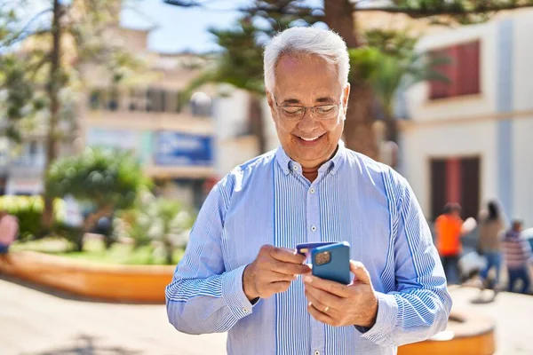 Senior man using smartphone and credit card at park
