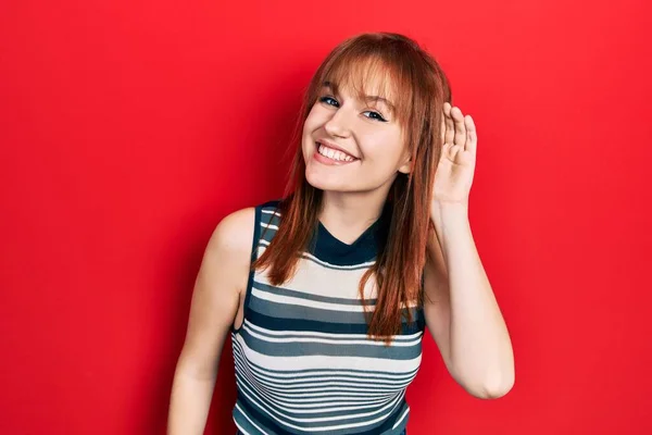 噂やゴシップに耳を傾ける耳の上に手で笑みを浮かべてカジュアルなTシャツを着て若い女性をRedhead 聴覚障害の概念 — ストック写真