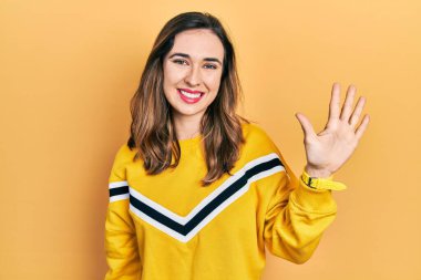 Gündelik kıyafetler giyen genç İspanyol kız beş numarayı gösterip işaret ederken kendinden emin ve mutlu gülümsüyor.. 