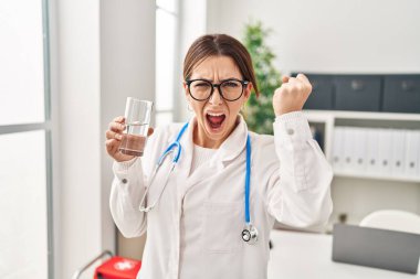 Elinde bir bardak su tutan genç esmer kadın öfkeyle bağırıyor, öfkeyle bağırıyor ve el kaldırıyor. 